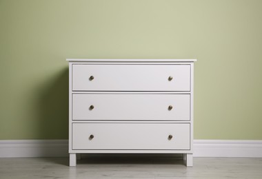 Photo of Modern white chest of drawers near light green wall indoors