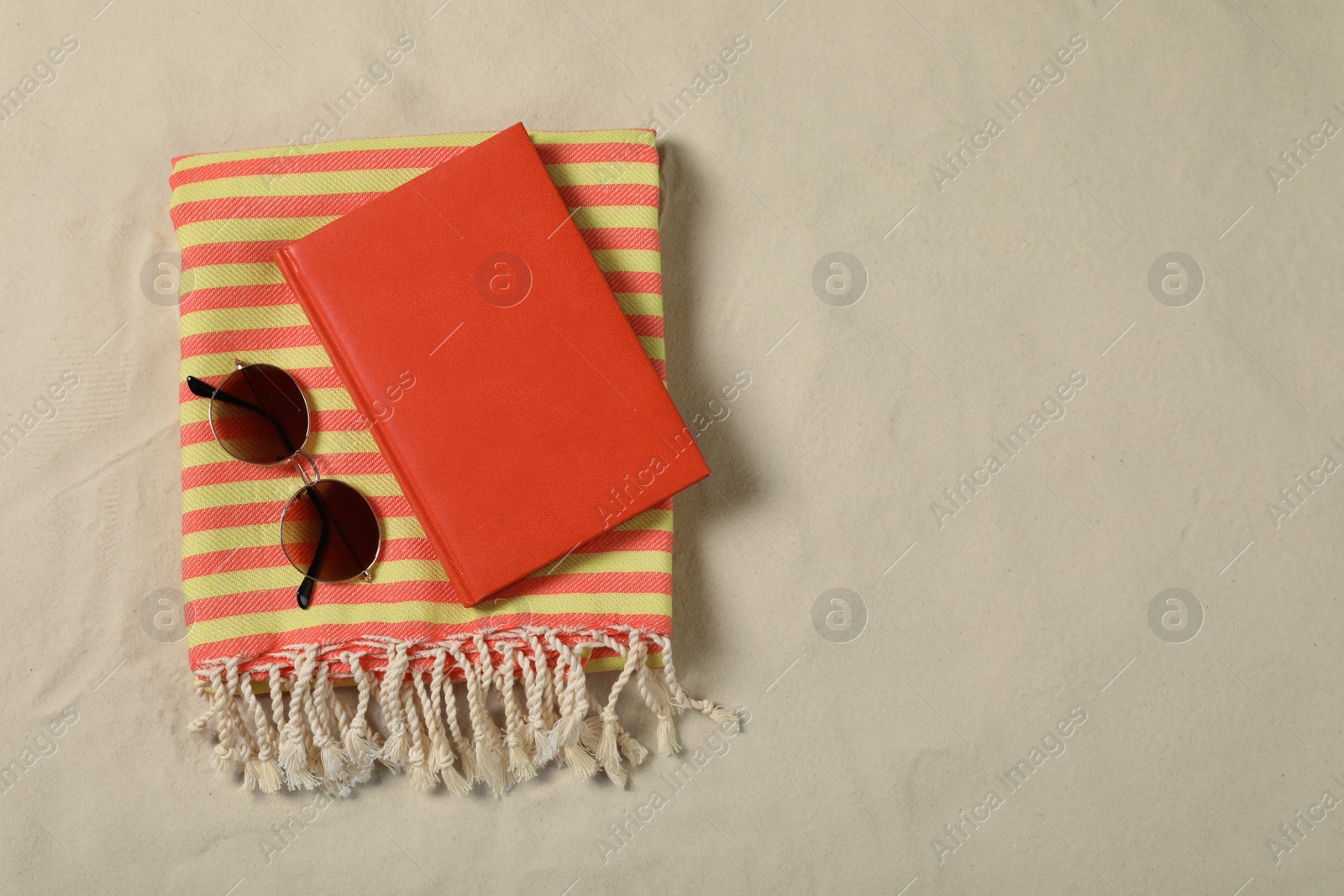 Photo of Beach towel, book and sunglasses on sand, top view. Space for text