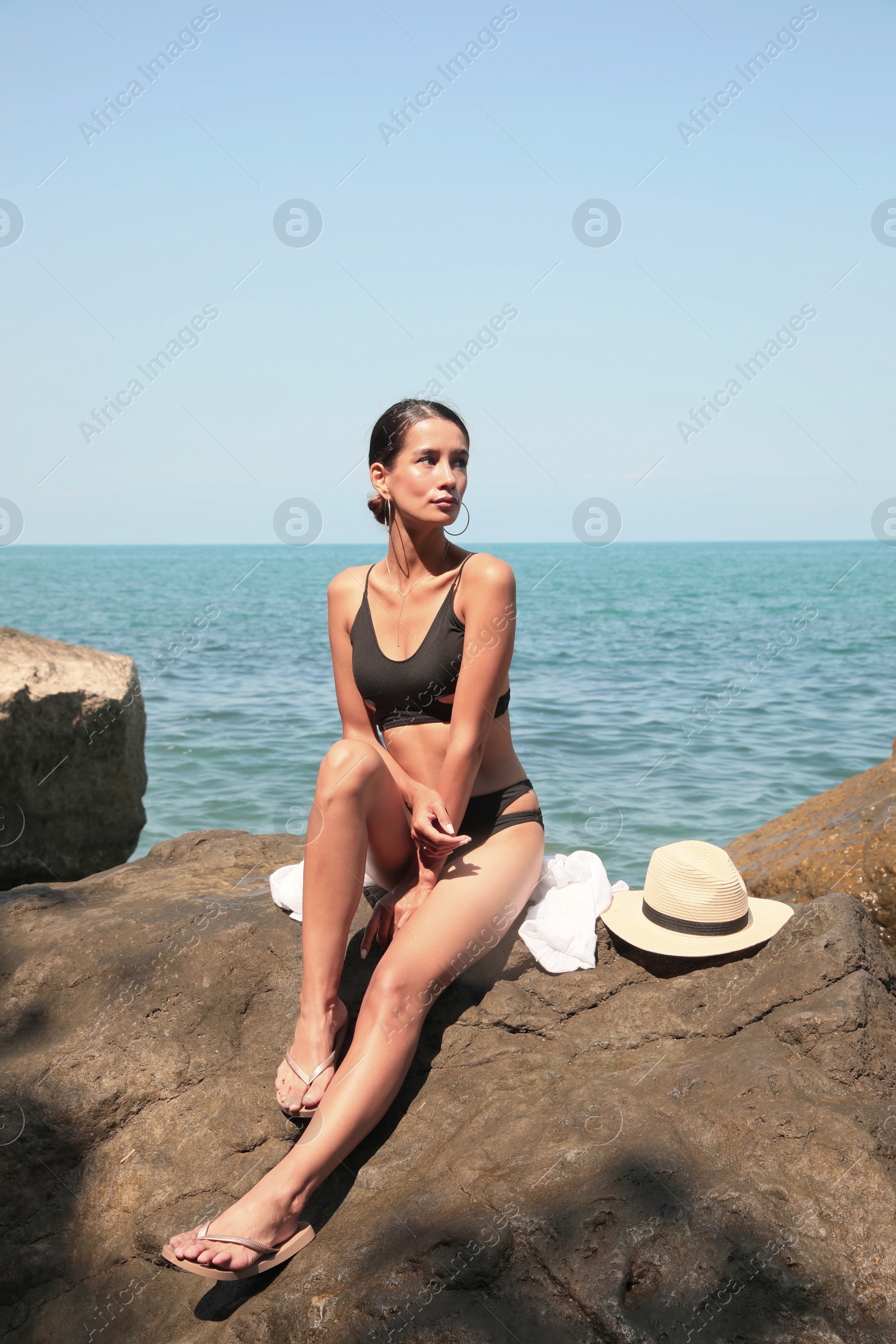 Photo of Beautiful young woman in stylish bikini sitting on rock near sea