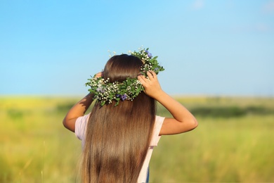 Cute little girl wearing flower wreath outdoors, back view. Child spending time in nature