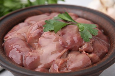 Photo of Bowl with raw chicken liver and parsley on table, closeup