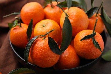 Fresh ripe tangerines with green leaves in bowl on table, closeup