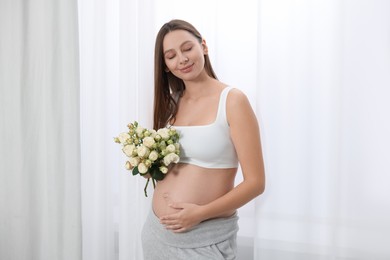 Photo of Beautiful pregnant woman with bouquet of roses near window indoors