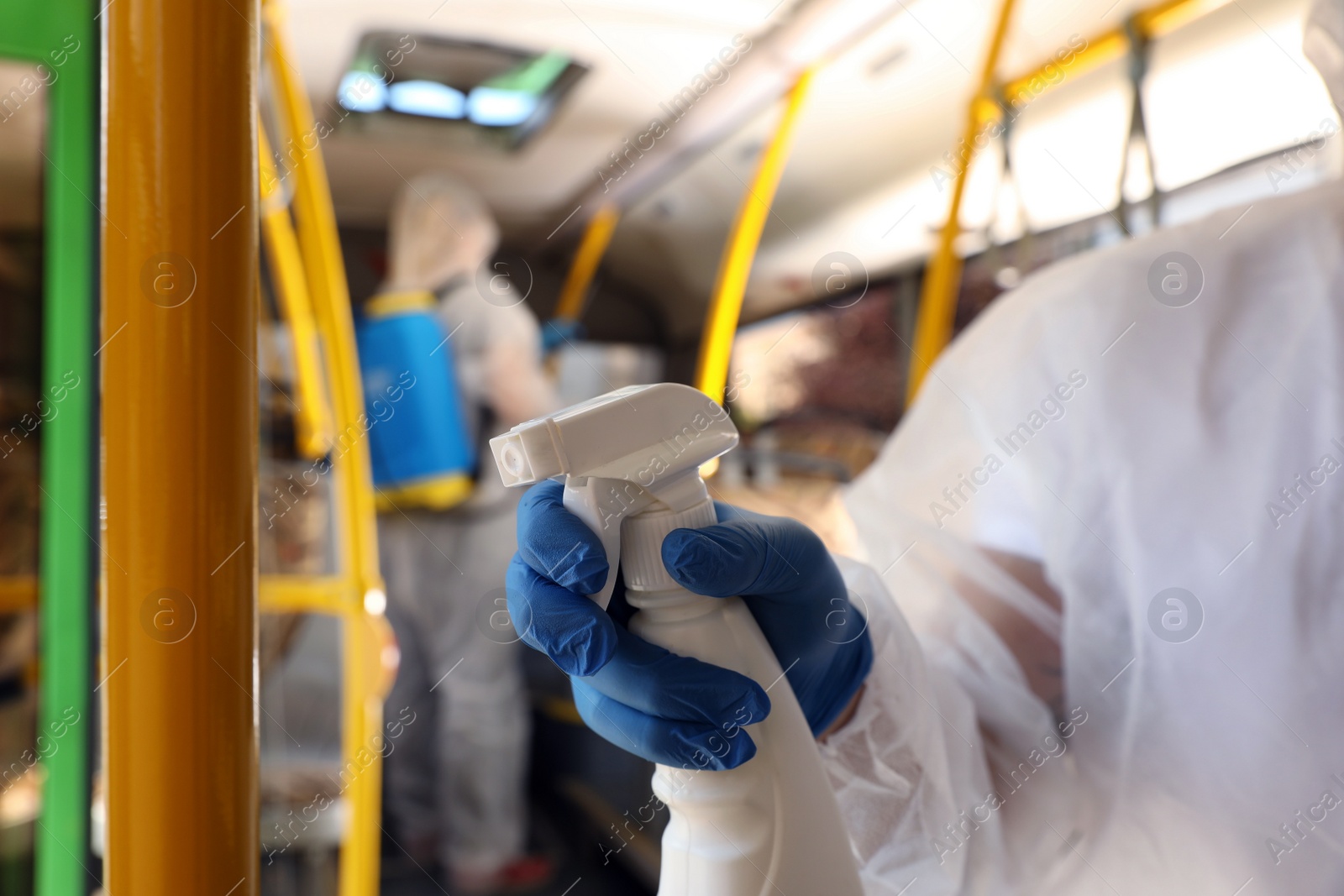 Photo of Public transport sanitation. Worker in protective suit disinfecting bus salon, closeup