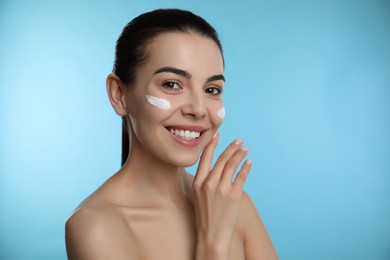 Photo of Young woman with cream on face against light blue background
