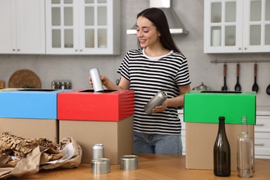 Photo of Garbage sorting. Smiling woman throwing metal can into cardboard box in kitchen