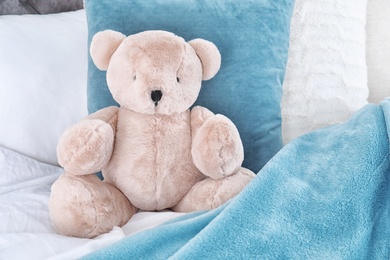 Photo of Cute teddy bear sitting on bed indoors. Space for text