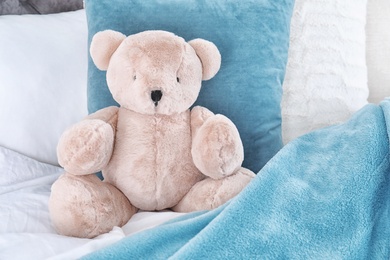 Cute teddy bear sitting on bed indoors. Space for text