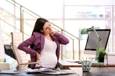 Photo of Young pregnant woman suffering from pain while working in office