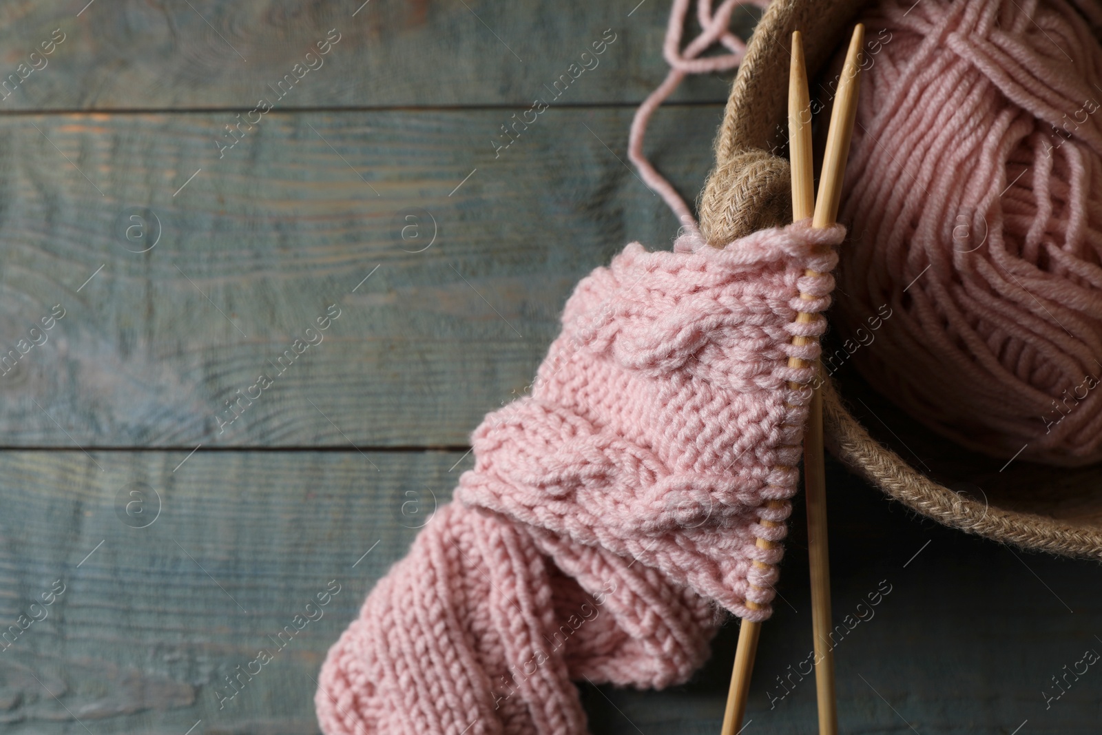 Photo of Soft pink woolen yarn, knitting and needles on wooden table, top view. Space for text