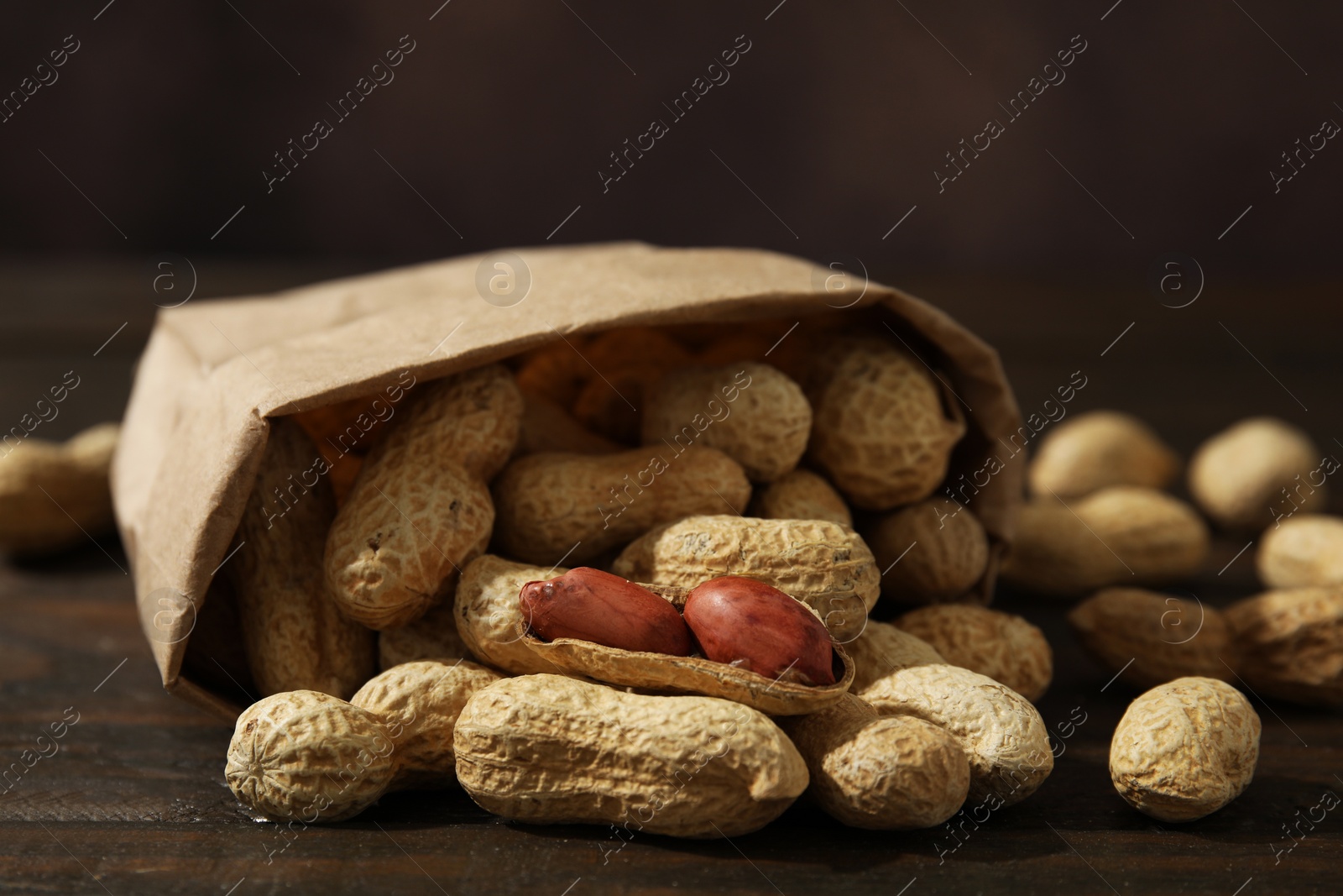 Photo of Paper bag with fresh unpeeled peanuts on wooden table, closeup