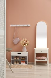 Hallway interior with mirror and white furniture near light pink wall. Stylish accessories