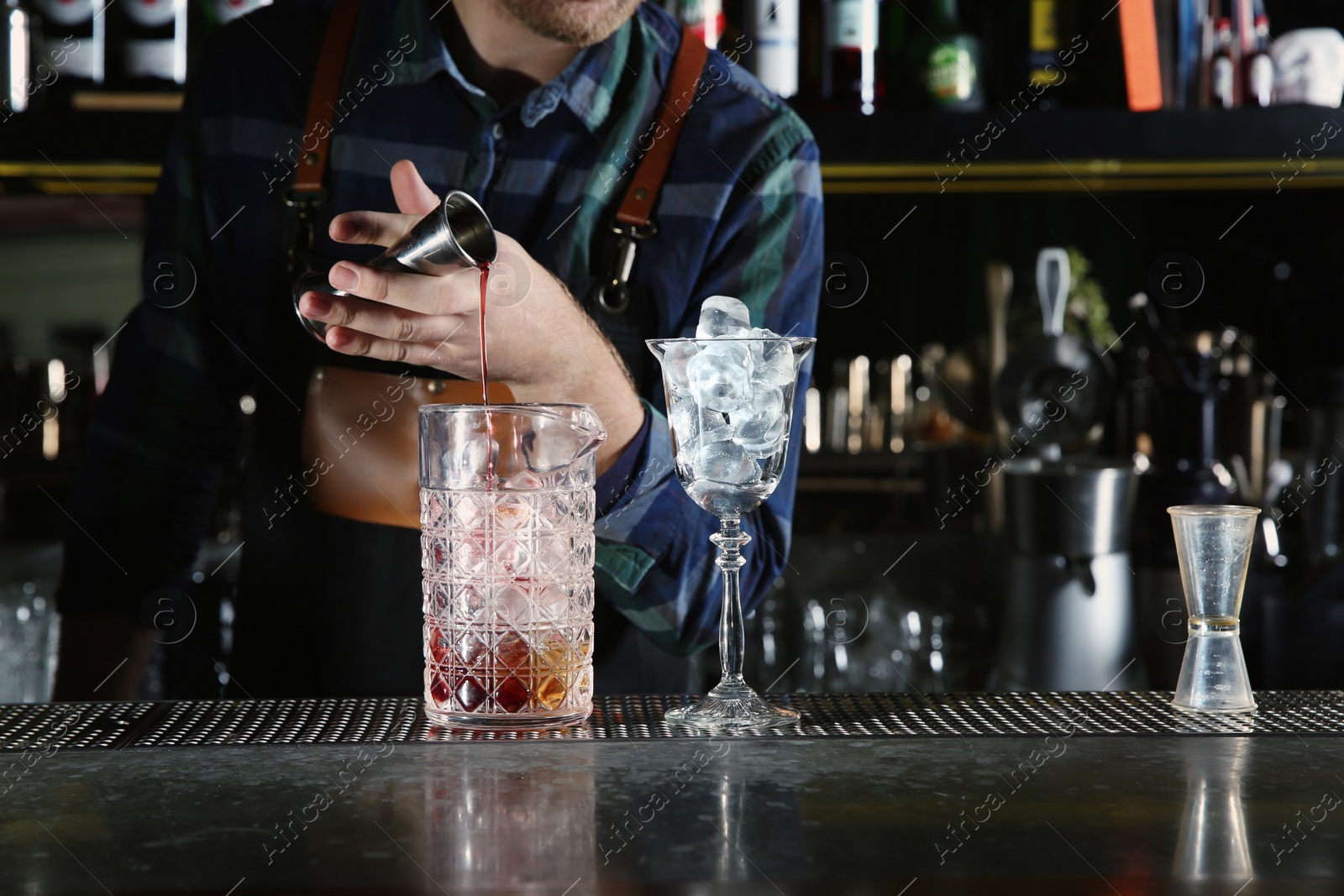 Photo of Barman pouring cocktail ingredients into mixing glass at counter in pub, closeup