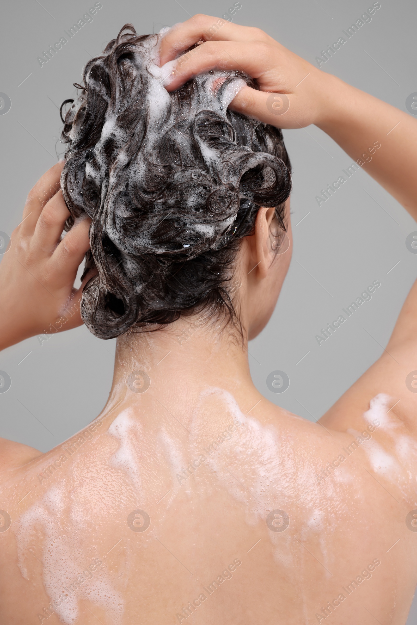 Photo of Woman washing hair on grey background, back view