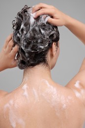 Photo of Woman washing hair on grey background, back view