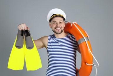 Photo of Happy sailor with orange ring buoy and swim fins on grey background