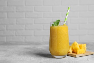 Glass of tasty pineapple smoothie and cut fruit on light gray table, space for text