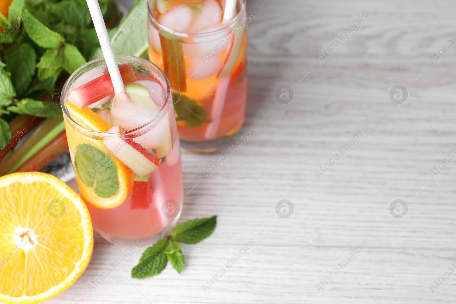 Photo of Tasty rhubarb cocktail with orange on white wooden table, space for text