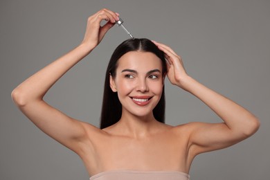 Photo of Beautiful woman applying hair serum on grey background. Cosmetic product
