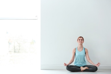 Beautiful woman meditating near wall indoors, space for text. Zen yoga