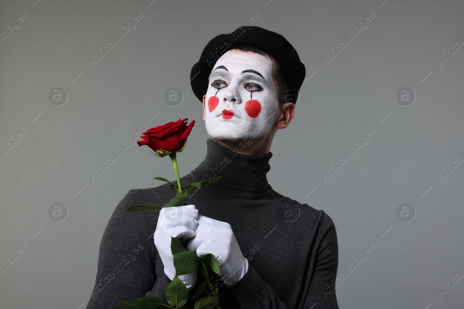 Photo of Portrait of mime artist with red rose on grey background