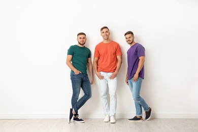 Photo of Group of young men in jeans and colorful t-shirts near light wall