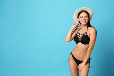 Photo of Beautiful young woman in stylish bikini with hat on light blue background. Space for text