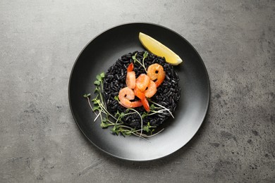 Delicious black risotto with shrimps and lemon on grey table, top view