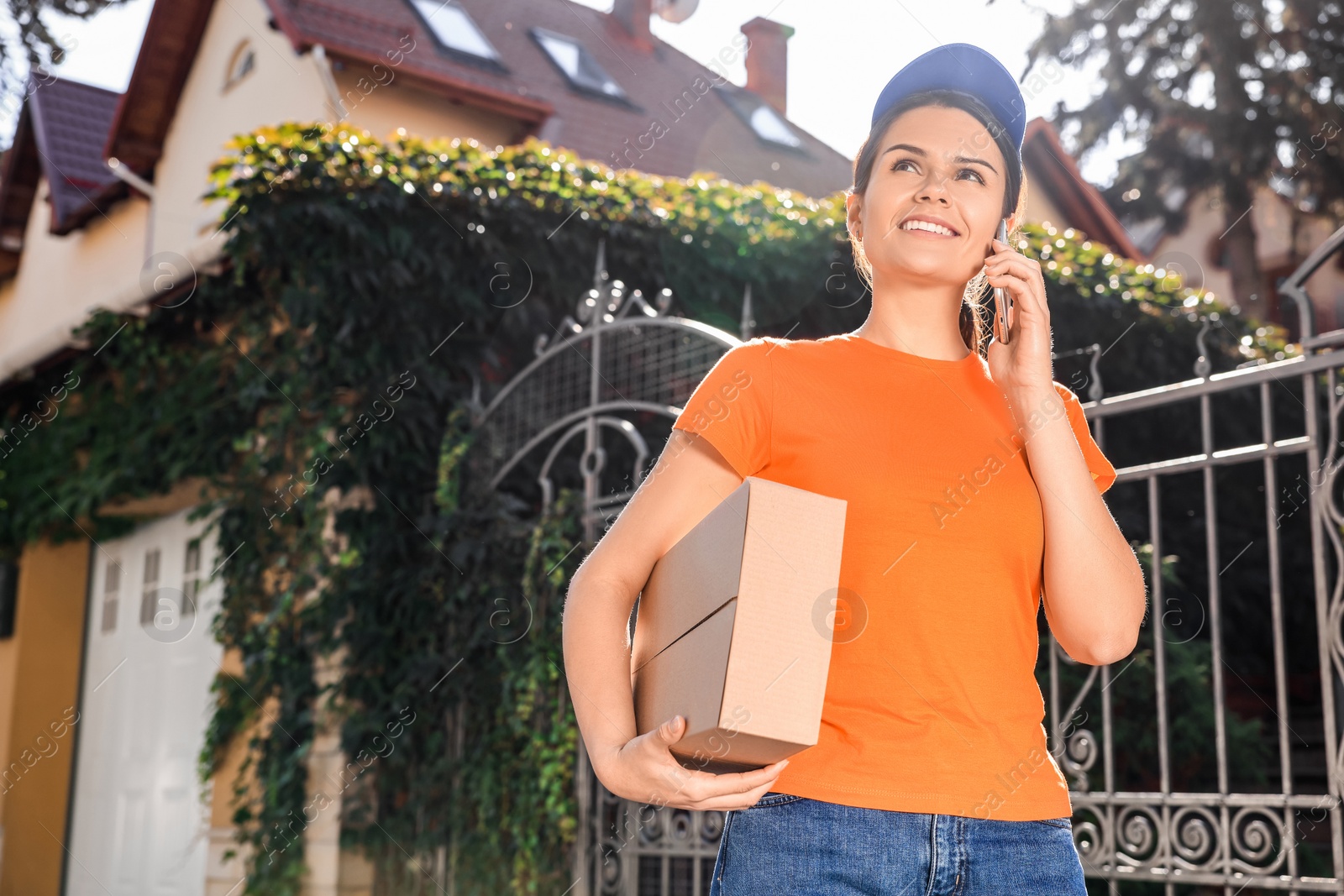 Photo of Courier with parcel talking by smartphone on city street