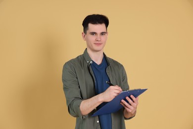 Photo of Handsome young man writing on clipboard against beige background