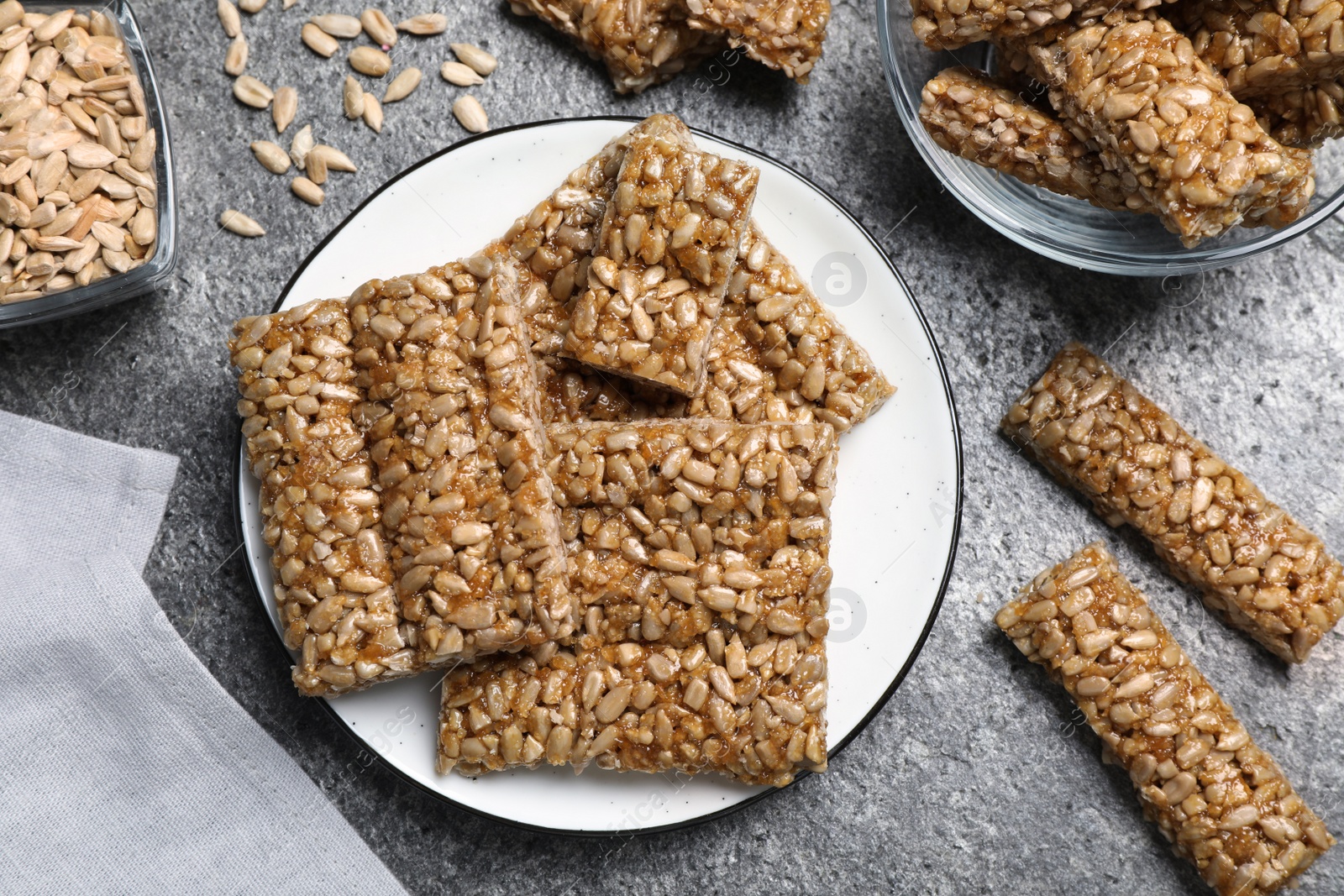 Photo of Delicious sweet kozinaki bars and sunflower seeds on grey table, flat lay