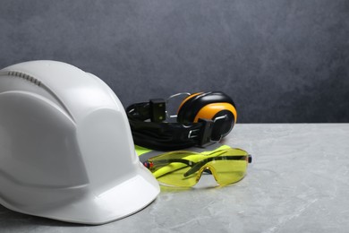 Hard hat, reflective vest, googles and earmuffs on grey surface. Space for text