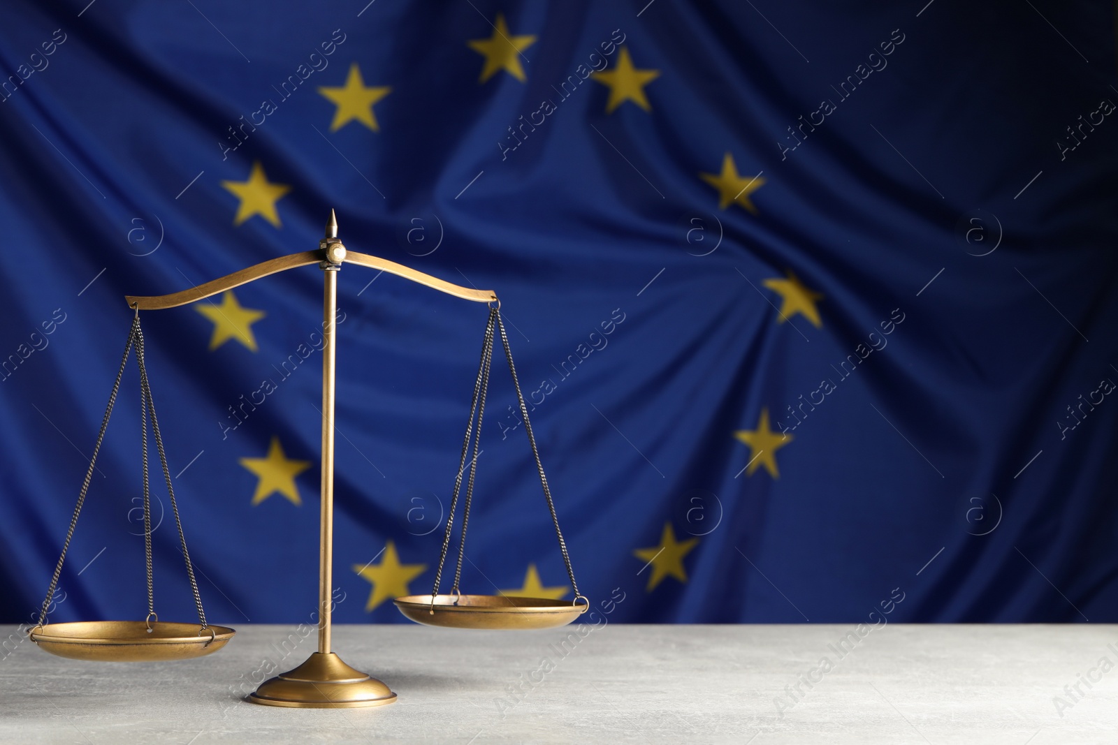 Photo of Scales of justice on light grey table against European Union flag. Space for text