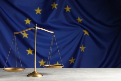 Photo of Scales of justice on light grey table against European Union flag. Space for text