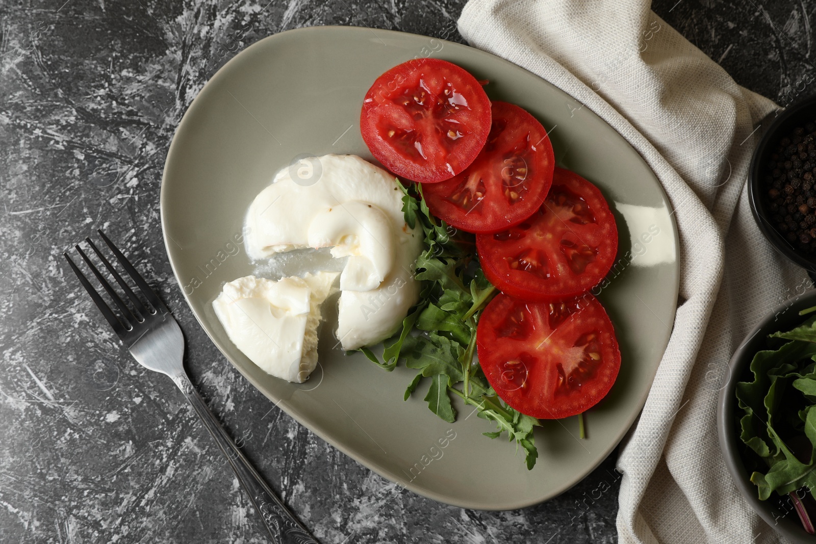 Photo of Delicious burrata cheese with tomatoes, arugula and fork on grey table, flat lay