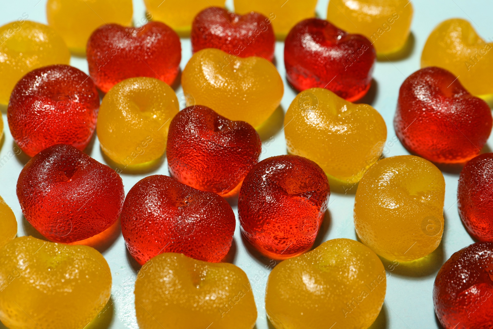 Photo of Delicious gummy cherry candies on light blue background, closeup