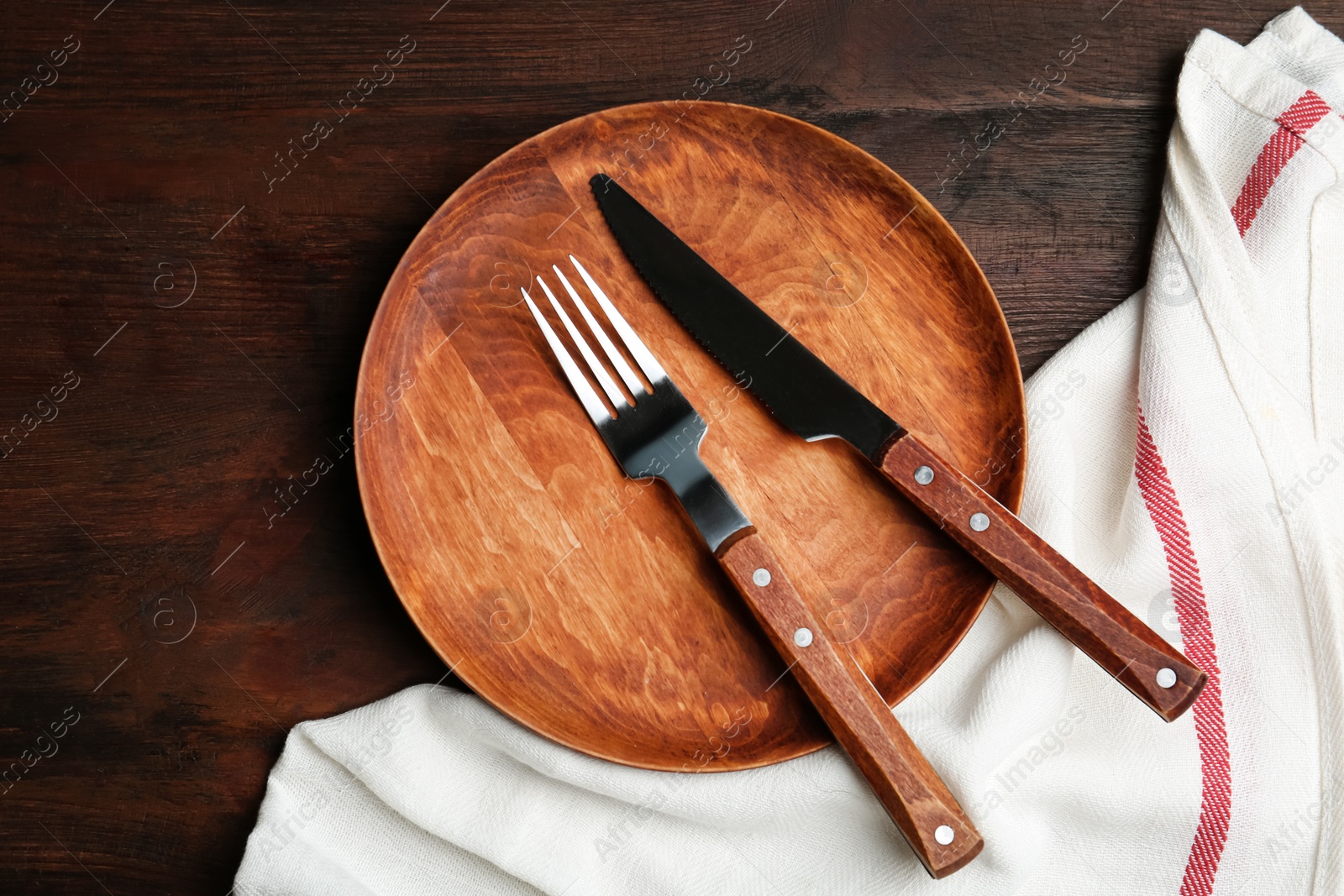 Photo of Plate with cutlery and white fabric on wooden table, flat lay