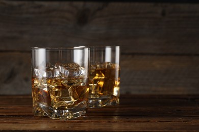 Photo of Whiskey with ice cubes in glasses on wooden table, closeup. Space for text