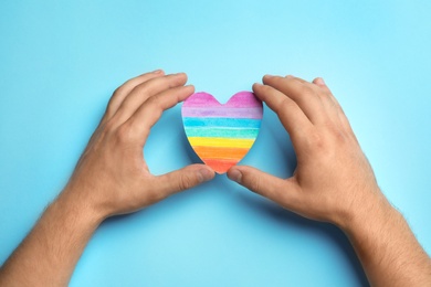 Photo of Man with rainbow heart on blue background, top view. Gay symbol