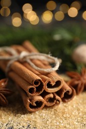 Photo of Different spices. Cinnamon sticks and cane sugar on table against blurred lights, closeup