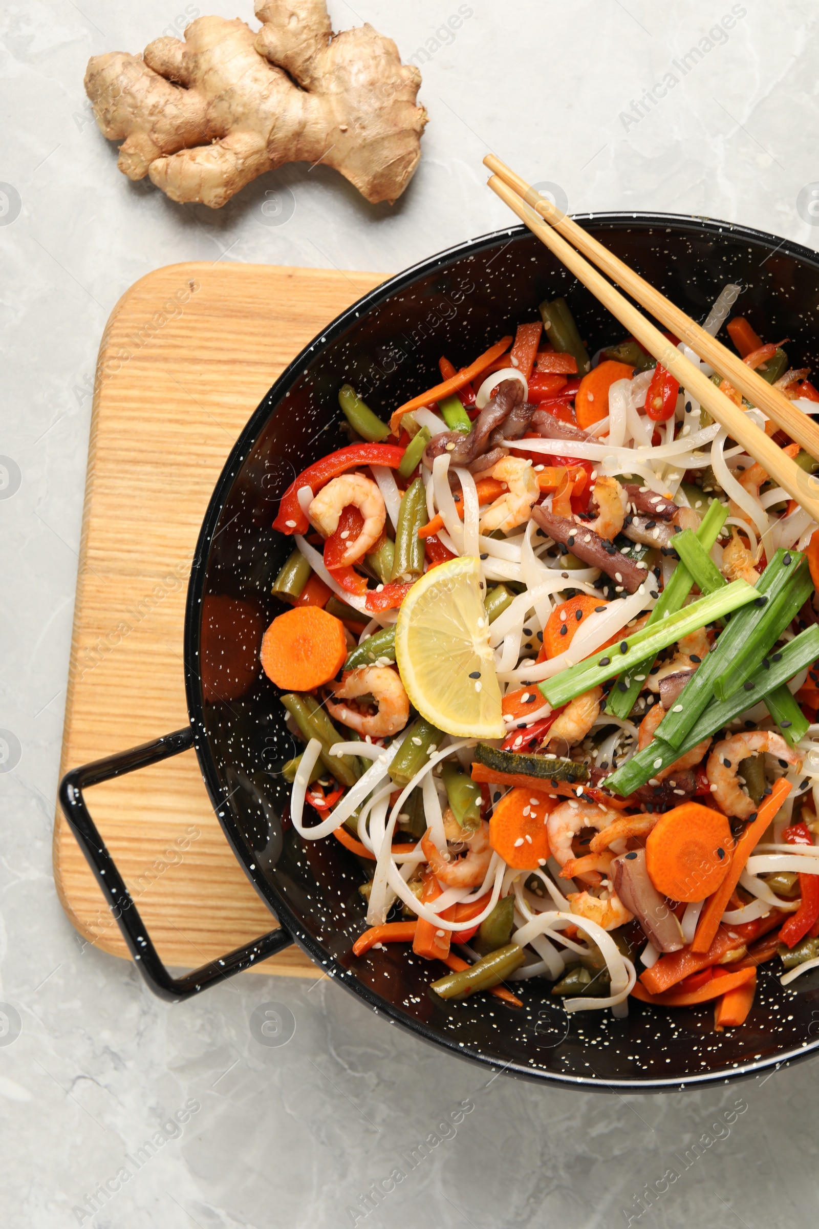 Photo of Shrimp stir fry with noodles and vegetables in wok on grey table, top view