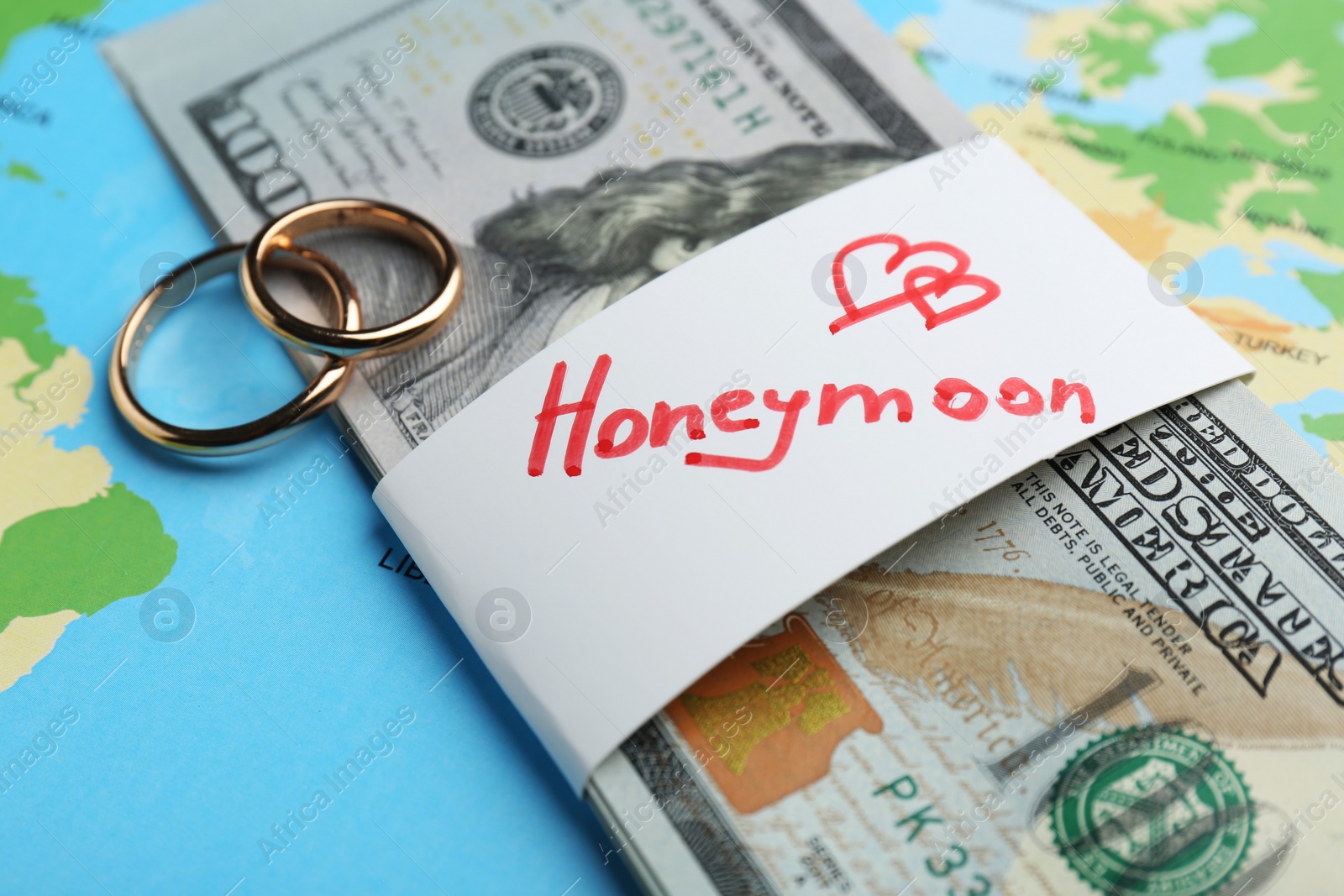 Photo of Two golden rings and stack of money with word Honeymoon on world map, closeup