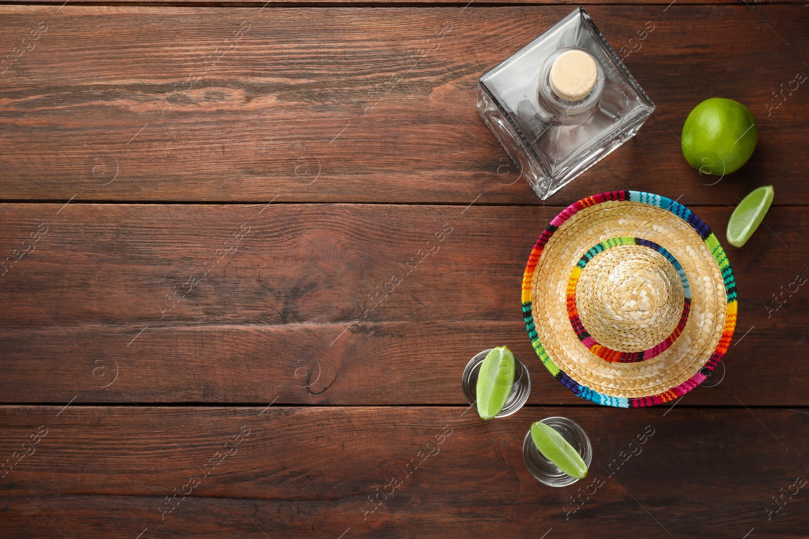 Photo of Mexican sombrero hat, tequila and lime on wooden table, flat lay. Space for text