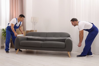 Workers wrapping sofa in stretch film indoors