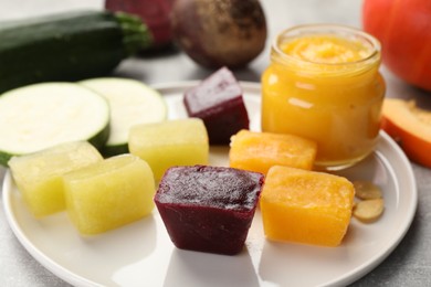 Photo of Frozen beet, pumpkin and zucchini puree cubes with ingredients on light grey table, closeup
