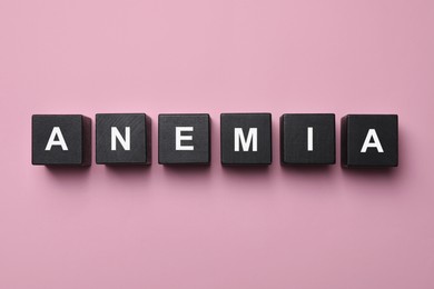 Photo of Word Anemia made with black wooden cubes on pink background, flat lay