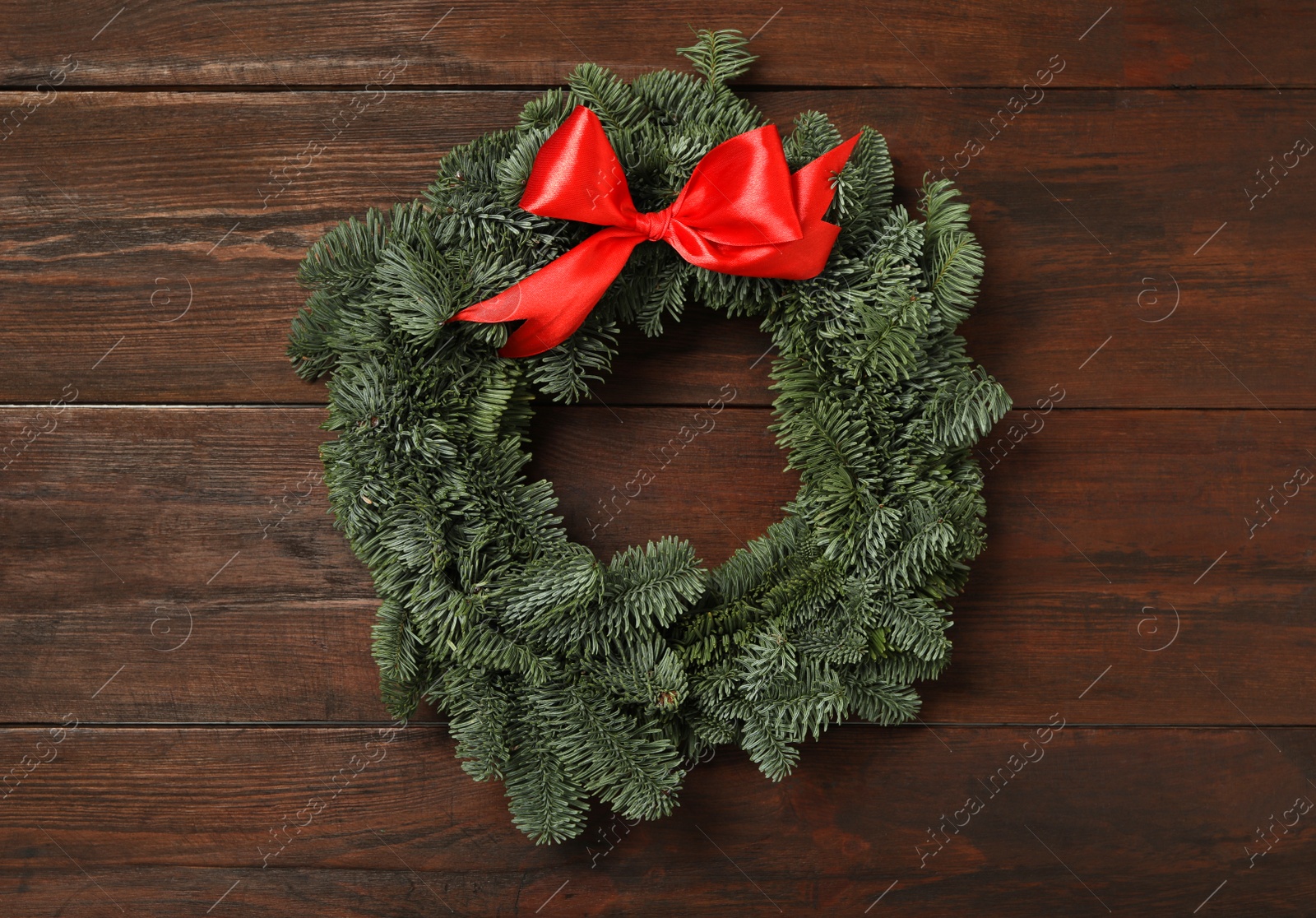 Photo of Christmas wreath made of fir tree branches with red ribbon on wooden background