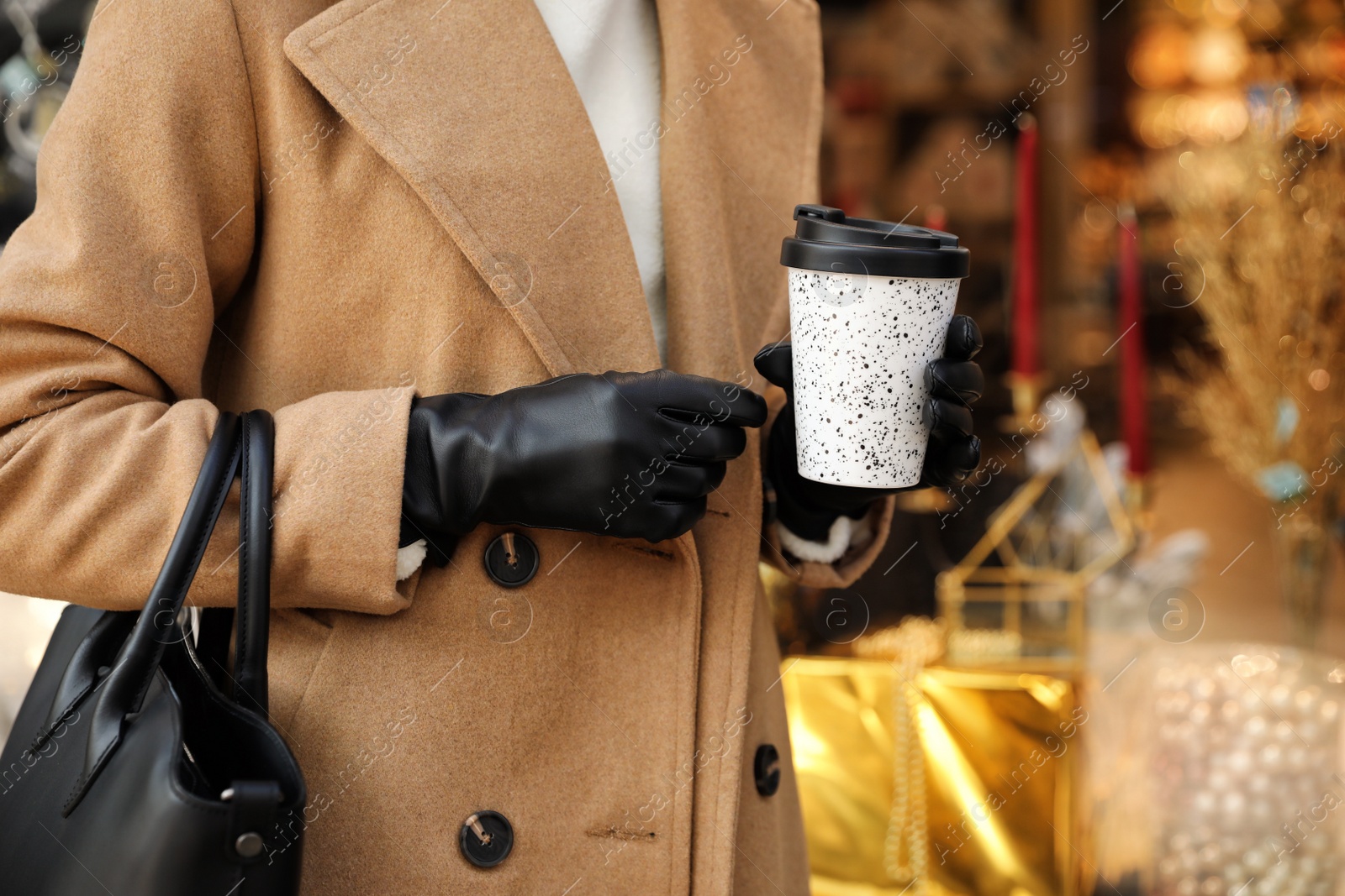 Photo of Woman with stylish leather gloves and cup of coffee near store decorated for Christmas, closeup