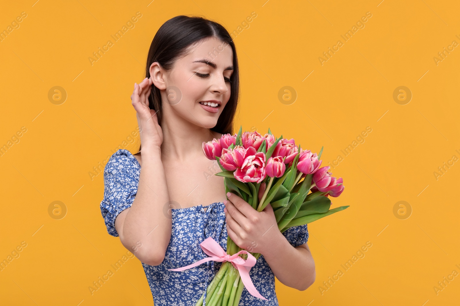 Photo of Happy young woman with beautiful bouquet on orange background