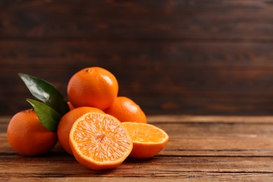 Fresh tangerines with green leaves on wooden table, closeup. Space for text